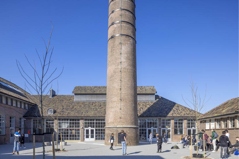 Schoolplein met oude schoorsteen en zicht op de gevel van de aula in het oude ketelhuis